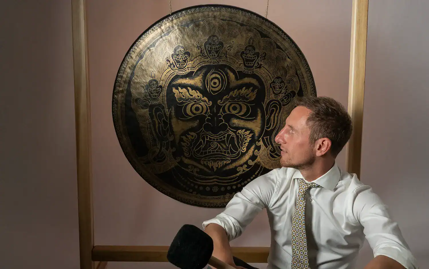 Jens Kemna in overhemd en stropdas met een mallet in zijn hand bij een grote gong